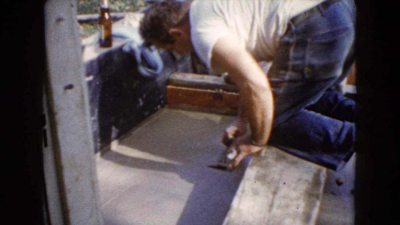 A man kneels at the edge of a cement patch, holding a trowel during a 1960 Wauconda home repair scene.