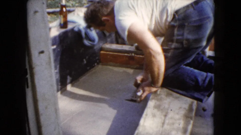 A man kneels at the edge of a cement patch, holding a trowel during a 1960 Wauconda home repair scene.