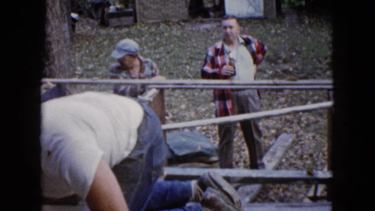 The final frame keeps the worker bent over the step in the foreground while two men stand outside the railing watching the work.