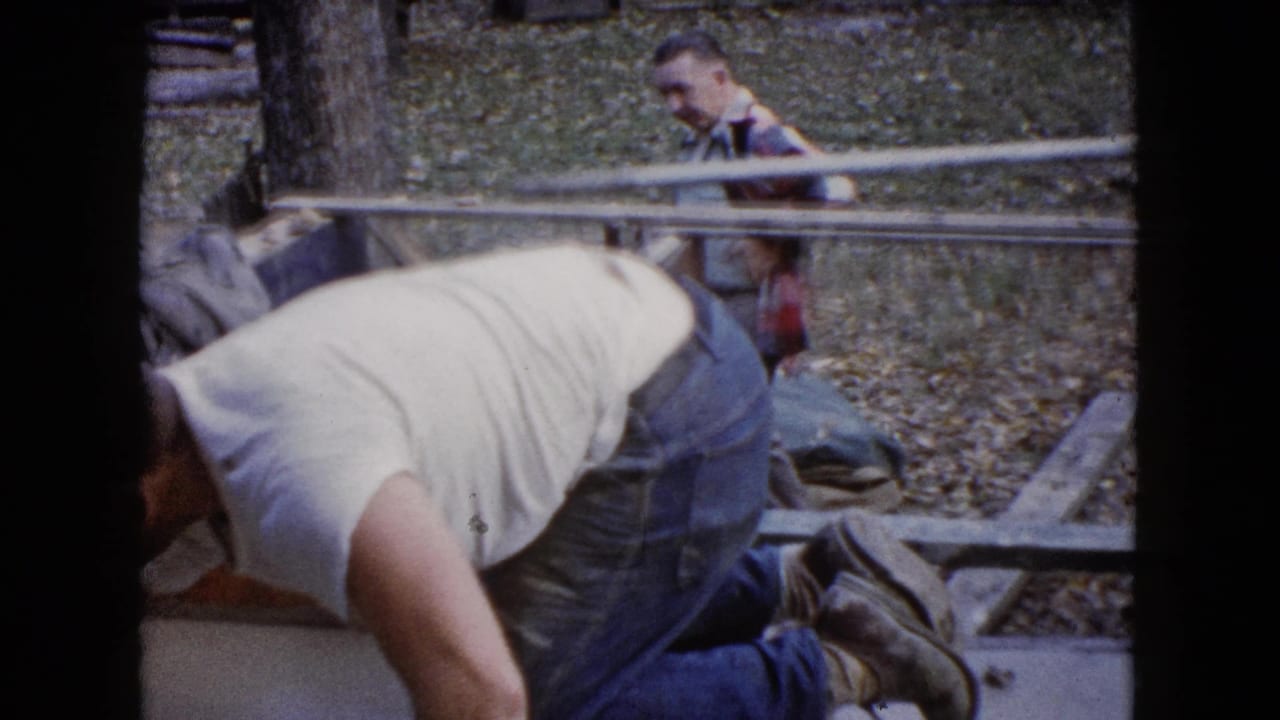 1960 Wauconda, Illinois still with a kneeling man beside boards and a second man partly visible behind the wood rail structure.