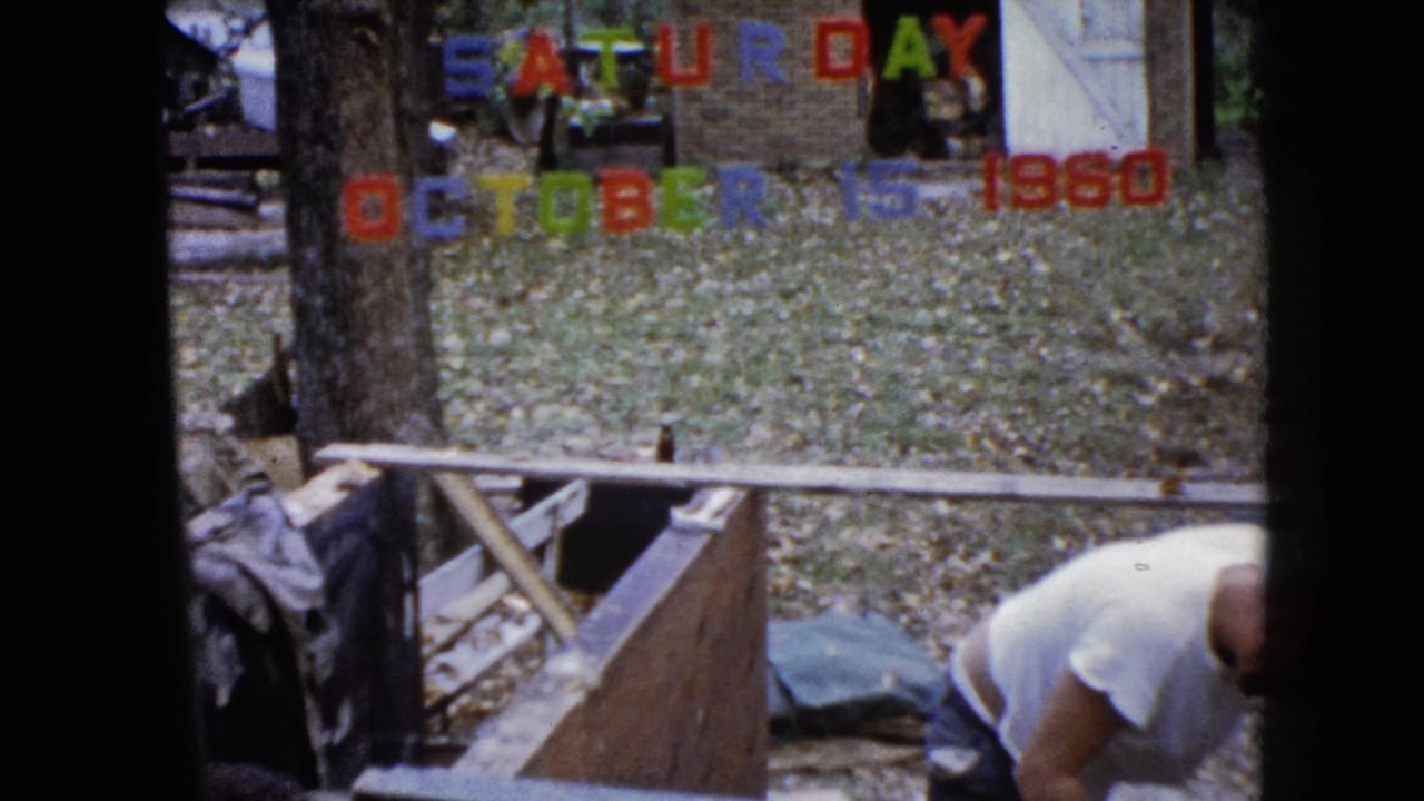 Man bends at the right edge near lumber and a backyard wooden frame.