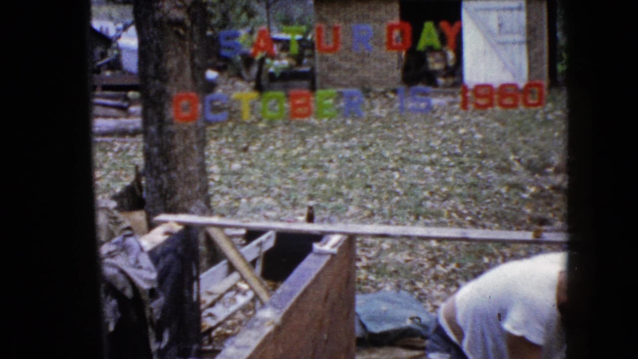 Dated 1960 home-movie view of a backyard work area in Wauconda with lumber, autumn leaves, and a man bending near the lower edge.