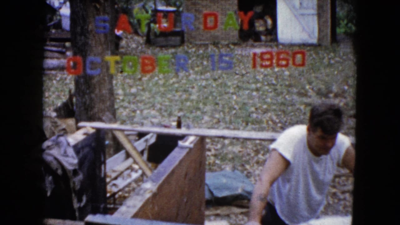 Man leans at the edge of a wooden structure in a backyard with date letters above.