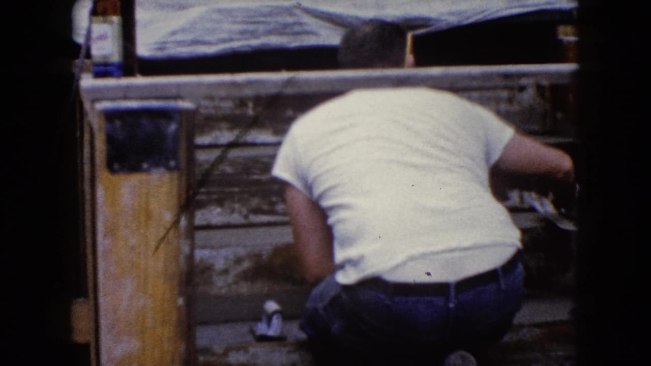 In Wauconda, Illinois around 1960, a man in a white T-shirt kneels close to weathered wooden steps while working with tools.