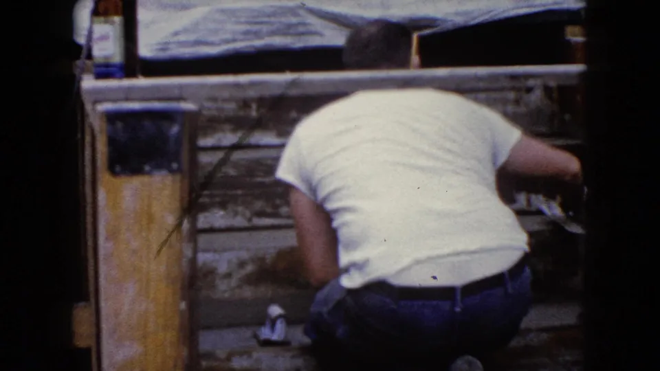 In Wauconda, Illinois around 1960, a man in a white T-shirt kneels close to weathered wooden steps while working with tools.