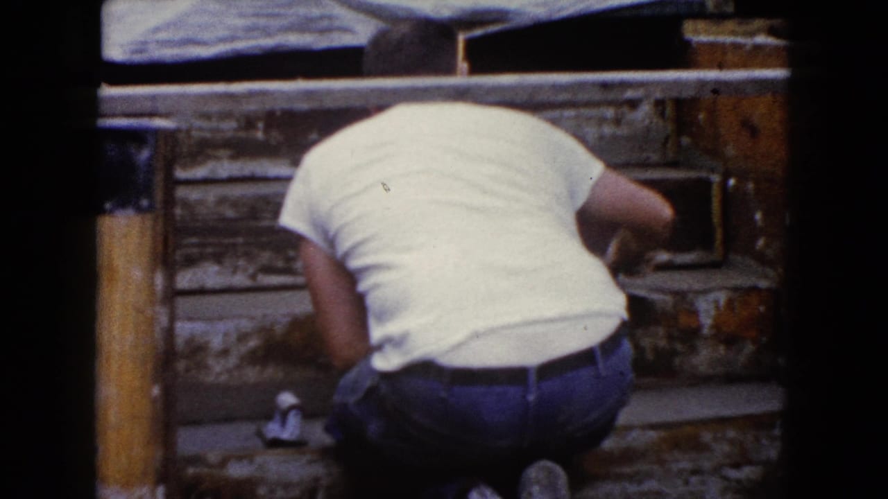Man bends over wooden steps, partly hidden by the frame edge and a dark divider.