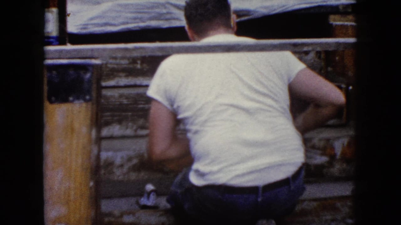 A closer rear view shows the man kneeling beside a wooden post and worn steps during the Wauconda, Illinois repair scene.