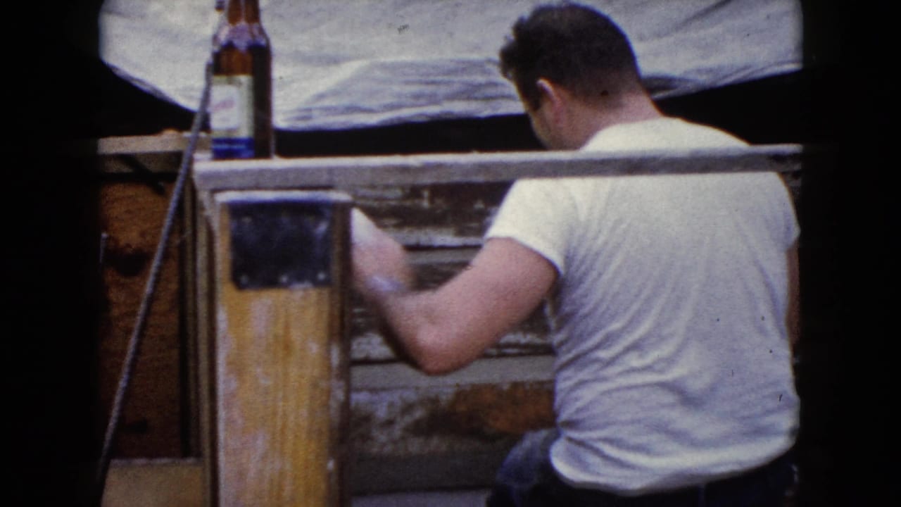 The man turns away while continuing work on the wooden structure, with the bottle still visible above the boards.