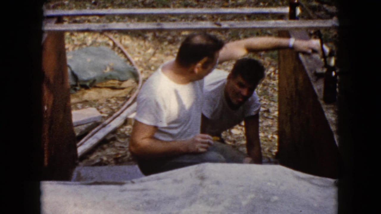 Two men appear in the Wauconda home-movie frame as one reaches toward the wooden form beside the concrete surface.