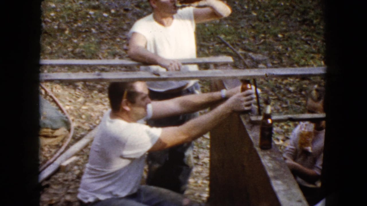 Two men in white shirts work around wooden forms and wet concrete outdoors.