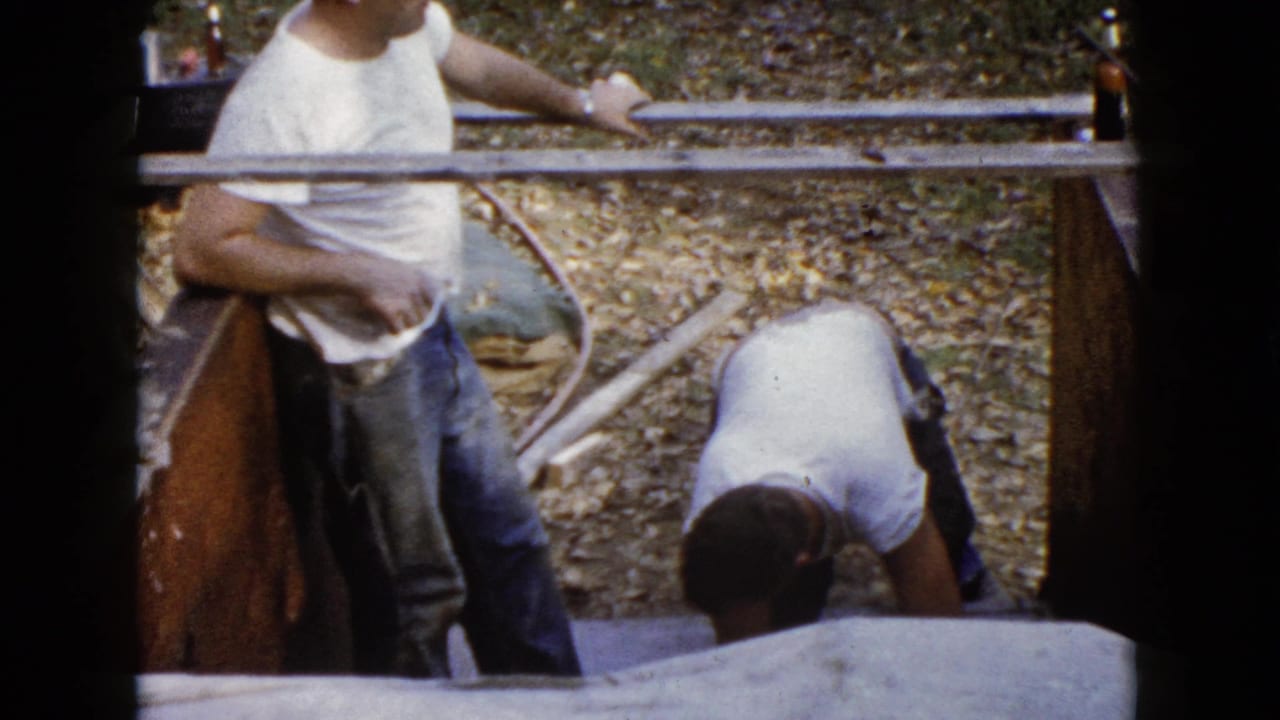 One man stands by wooden forms while another bends over the concrete work area.