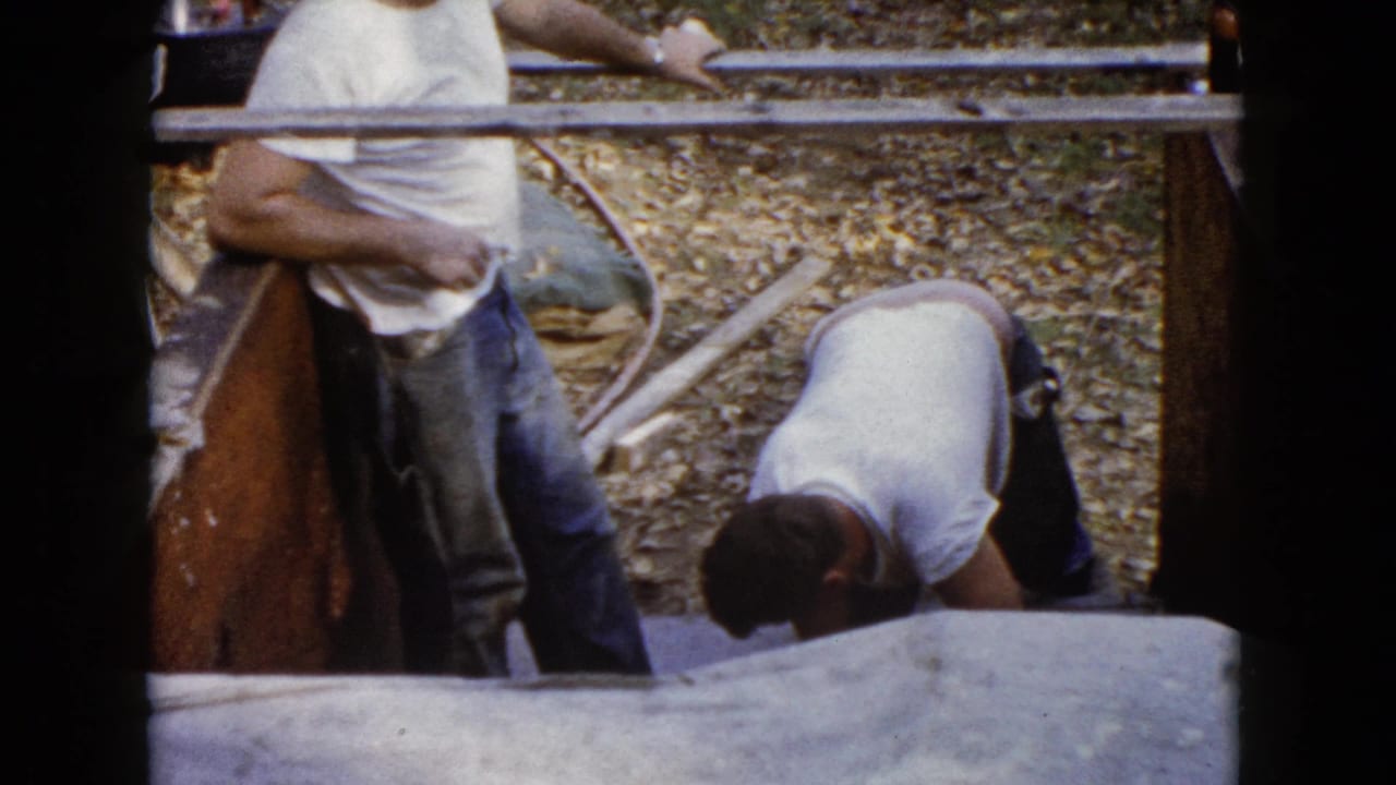 The home-movie frame shows a worker leaning at the form as another man bends near the wet concrete steps in Wauconda.