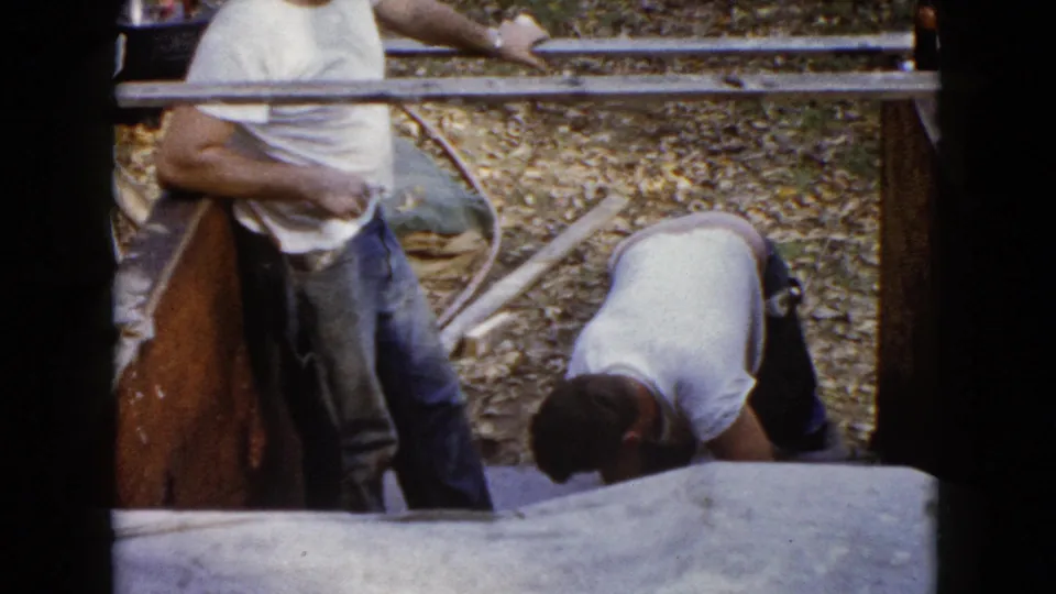 The home-movie frame shows a worker leaning at the form as another man bends near the wet concrete steps in Wauconda.