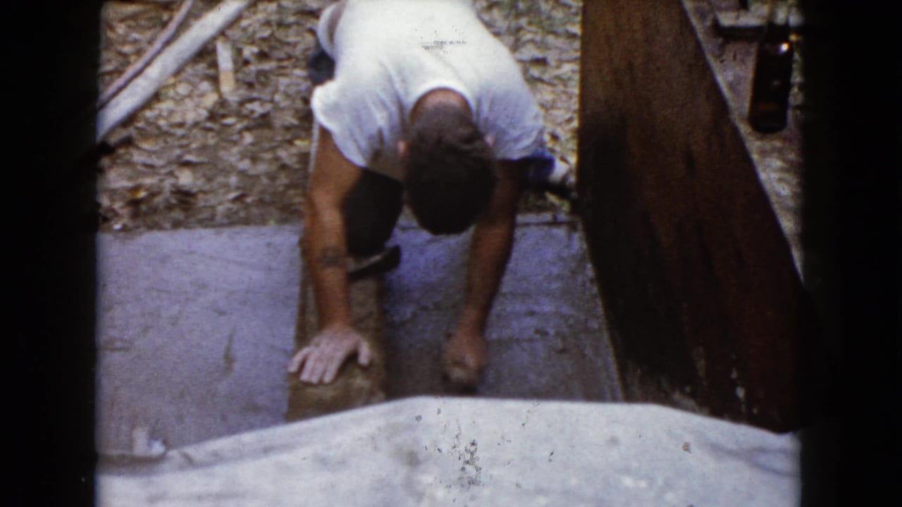 A man leans over fresh concrete steps within wooden forms, his hands near the surface as he continues the finishing work.