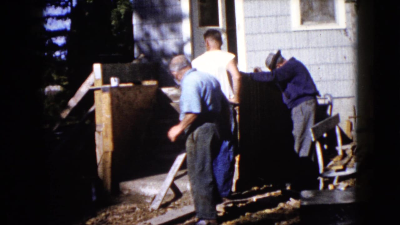 Adult men work beside wooden planks near the entrance of a house.