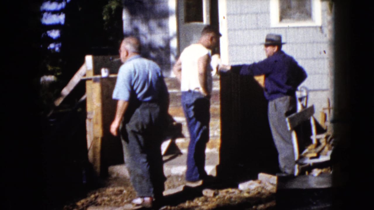 Adult men in casual clothes work and confer near exterior woodwork at a Wauconda, Illinois home in 1960.