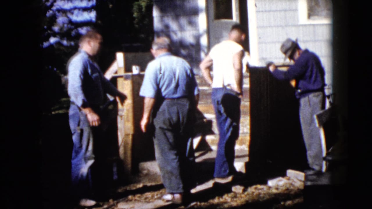 Men stand near front steps with a large wooden piece outside a house.