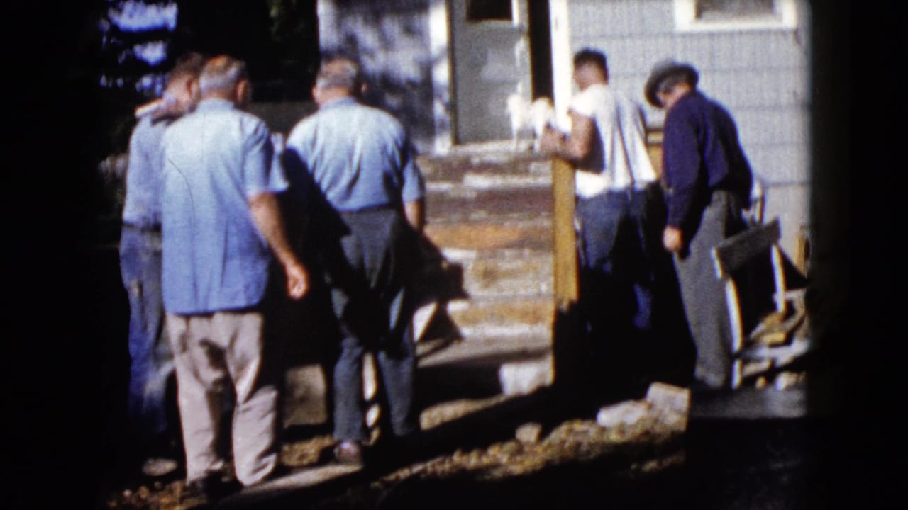 In Wauconda, Illinois, 1960, four adult men appear to work around a wooden porch beside a house in bright daylight.