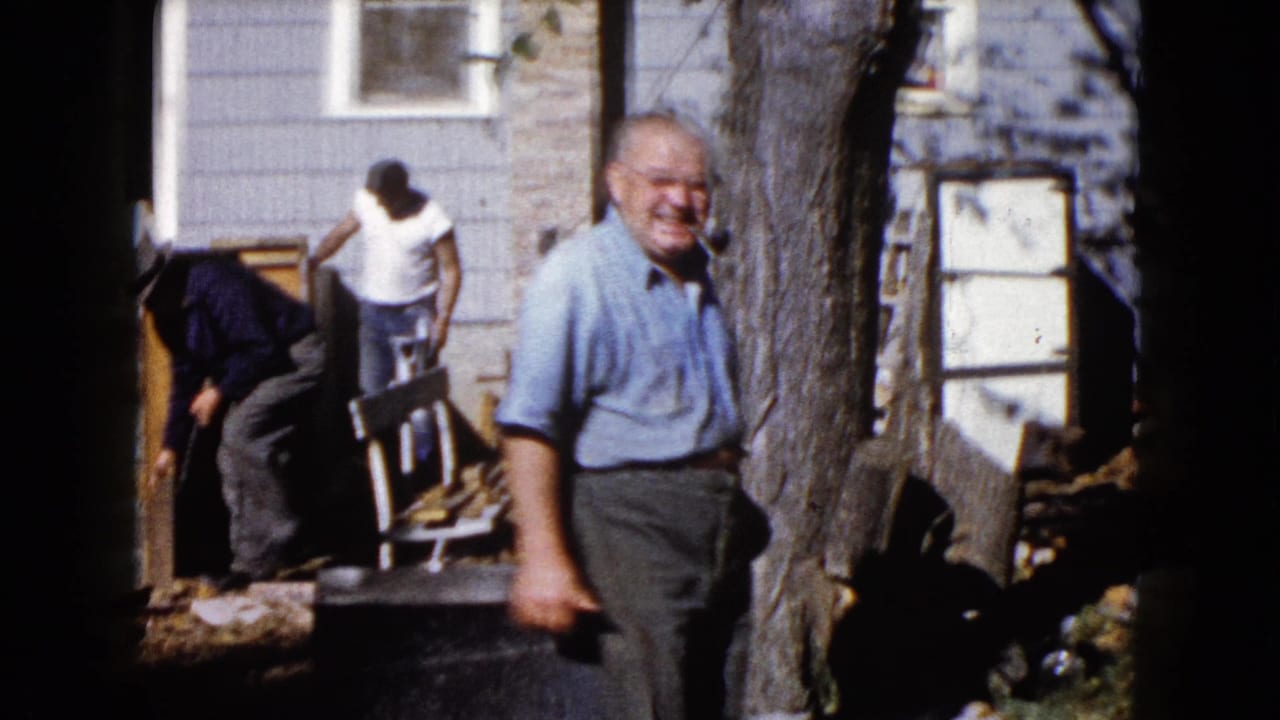1960 Wauconda frame with a smiling man near a tree trunk and other men working around porch materials at a residential exterior.