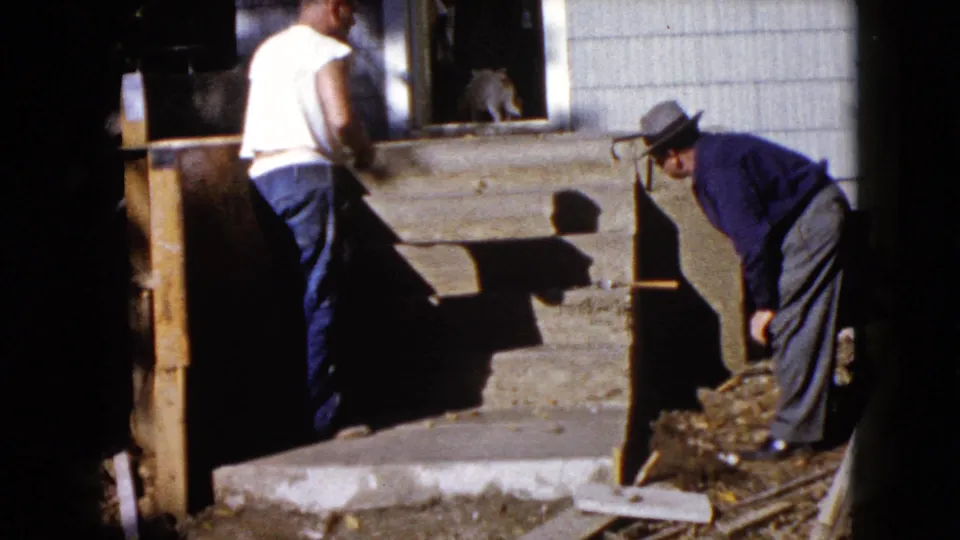Two men remain beside the exterior steps, one standing and one bending, in a candid 1960 Wauconda house-repair moment.
