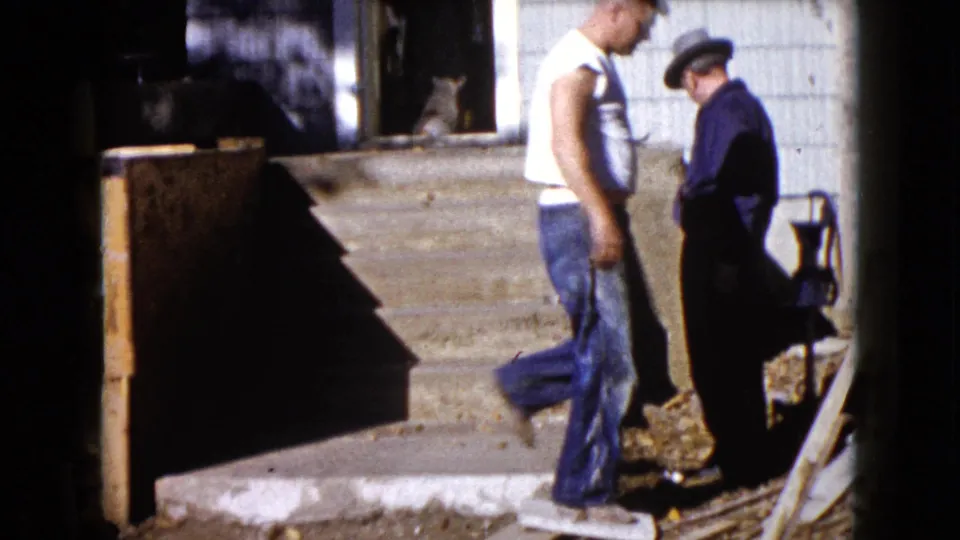 The home-movie frame shows a man moving across the porch area during outdoor house work in Wauconda, Illinois, in 1960.