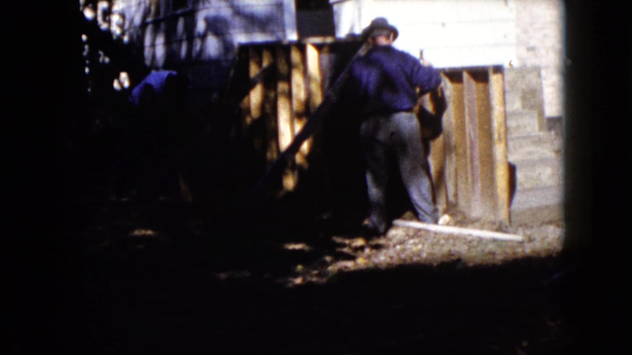 Two men work beside wooden boards and concrete steps in strong sunlight and shade.