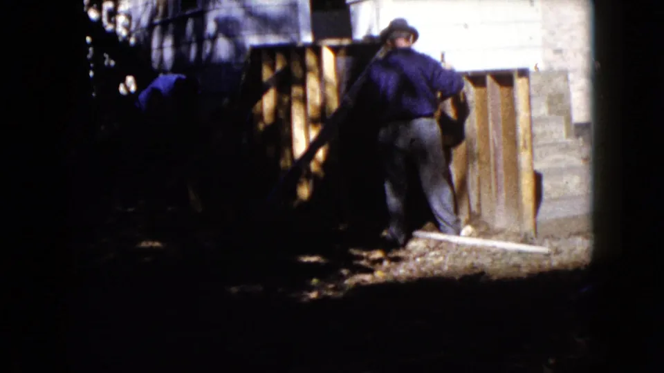 In Wauconda, Illinois, 1960, two men appear to work on a house structure near wooden boards and concrete steps.