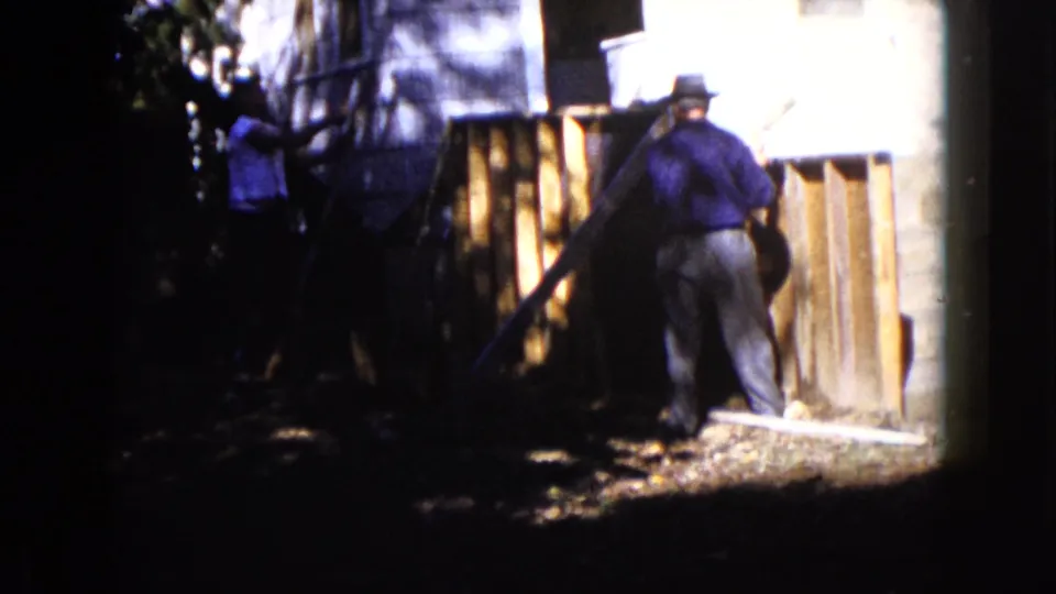 In 1960 Wauconda, Illinois, men appear to work near a wooden outdoor structure beside a light-sided house.