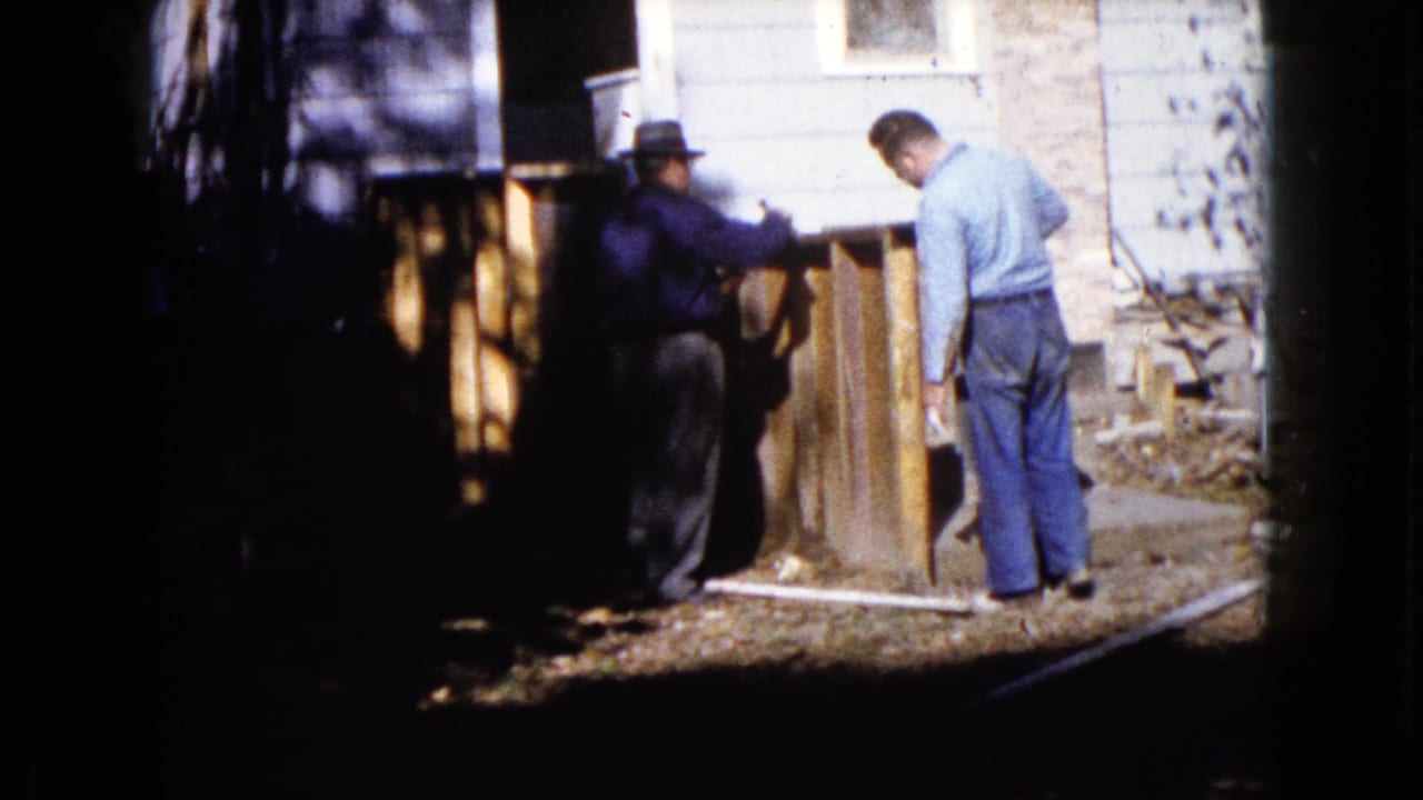 Two adult men appear to position wood panels in a residential yard in 1960 Wauconda home-movie footage.