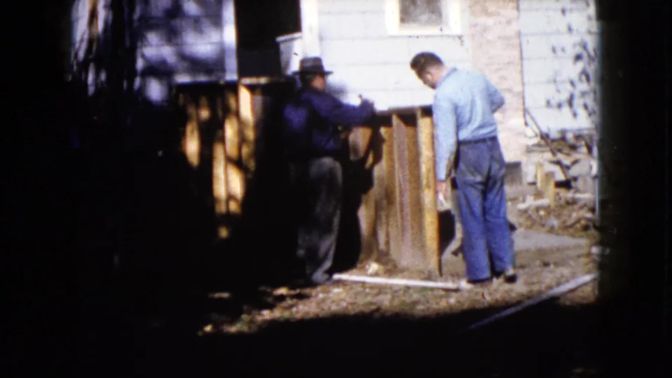 Two adult men appear to position wood panels in a residential yard in 1960 Wauconda home-movie footage.
