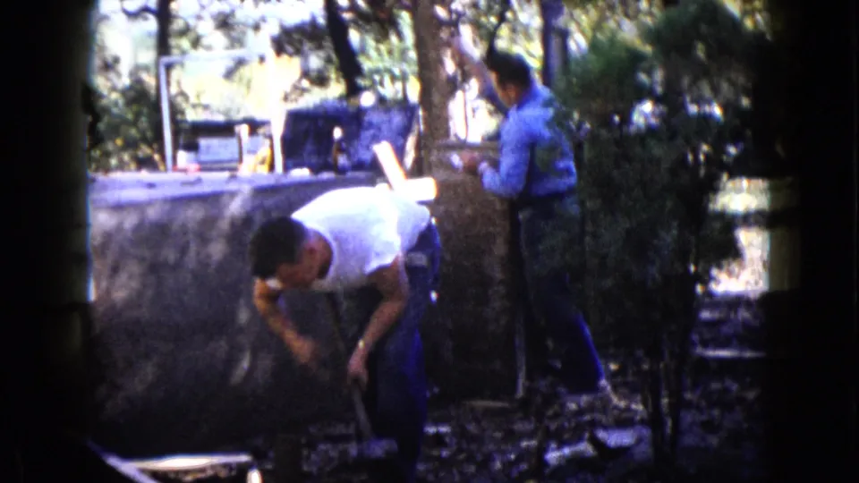 The 8mm frame shows one man bent over with a tool and another standing near a tree in a Wauconda backyard.