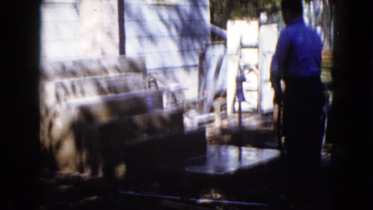 Man in a blue shirt stands near wet concrete steps beside a house wall.