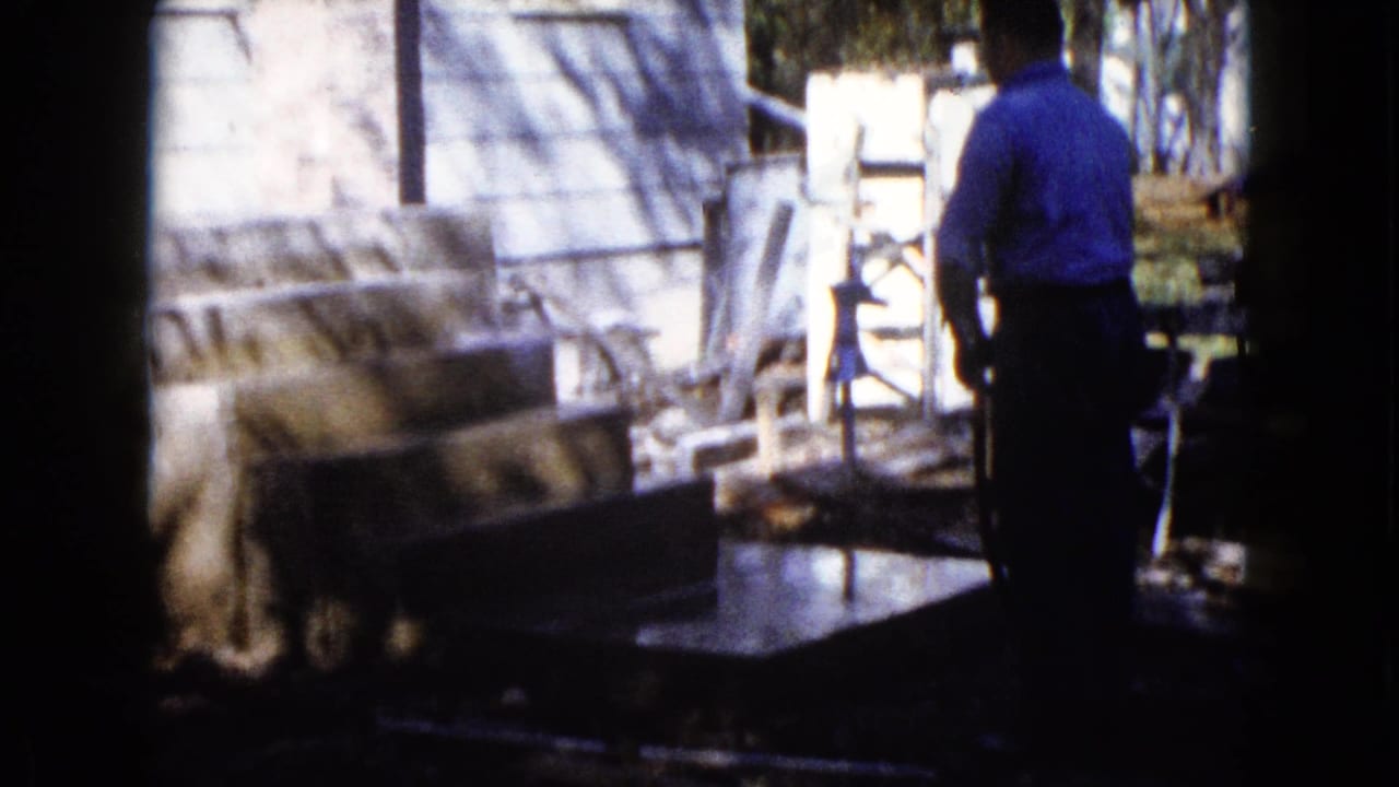 In Wauconda, Illinois, circa 1960, a man stands by a house while water is sprayed over fresh concrete near a porch or step area.