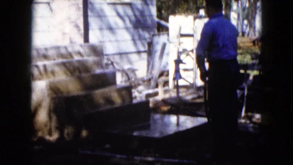 In Wauconda, Illinois, circa 1960, a man stands by a house while water is sprayed over fresh concrete near a porch or step area.