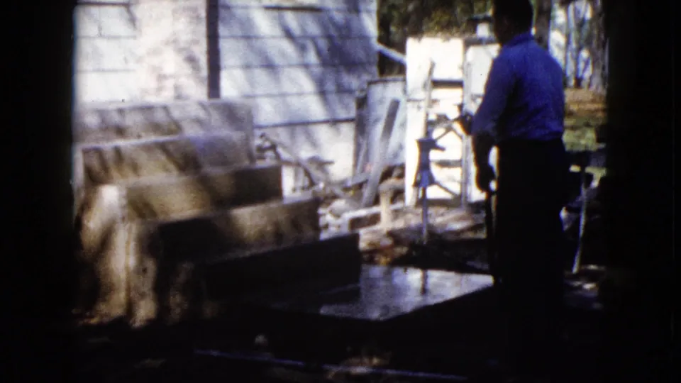 A backyard construction moment shows the man near the hose and concrete porch area, with yard objects and house siding visible.