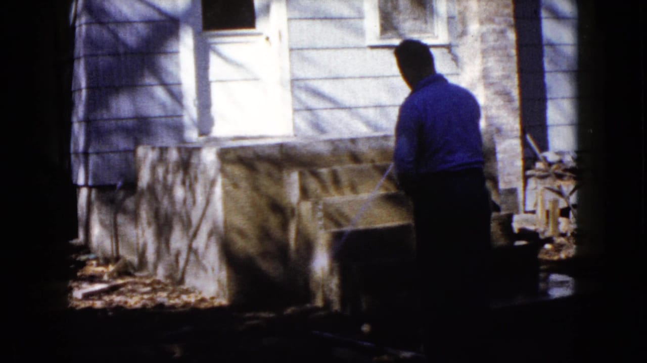 In Wauconda, Illinois in 1960, a man waters newly built concrete steps beside light-colored house siding and a white door.