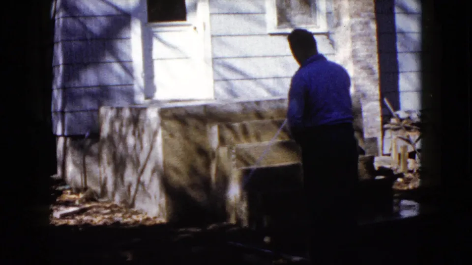 In Wauconda, Illinois in 1960, a man waters newly built concrete steps beside light-colored house siding and a white door.