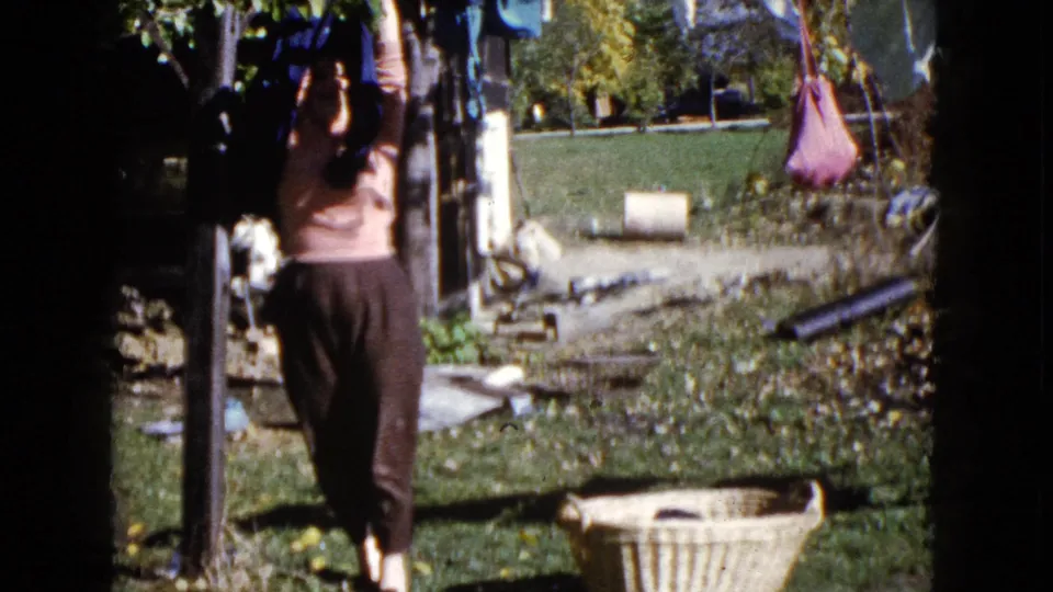 A woman seen from behind hangs laundry on an outdoor line in 1960 Wauconda home-movie footage.