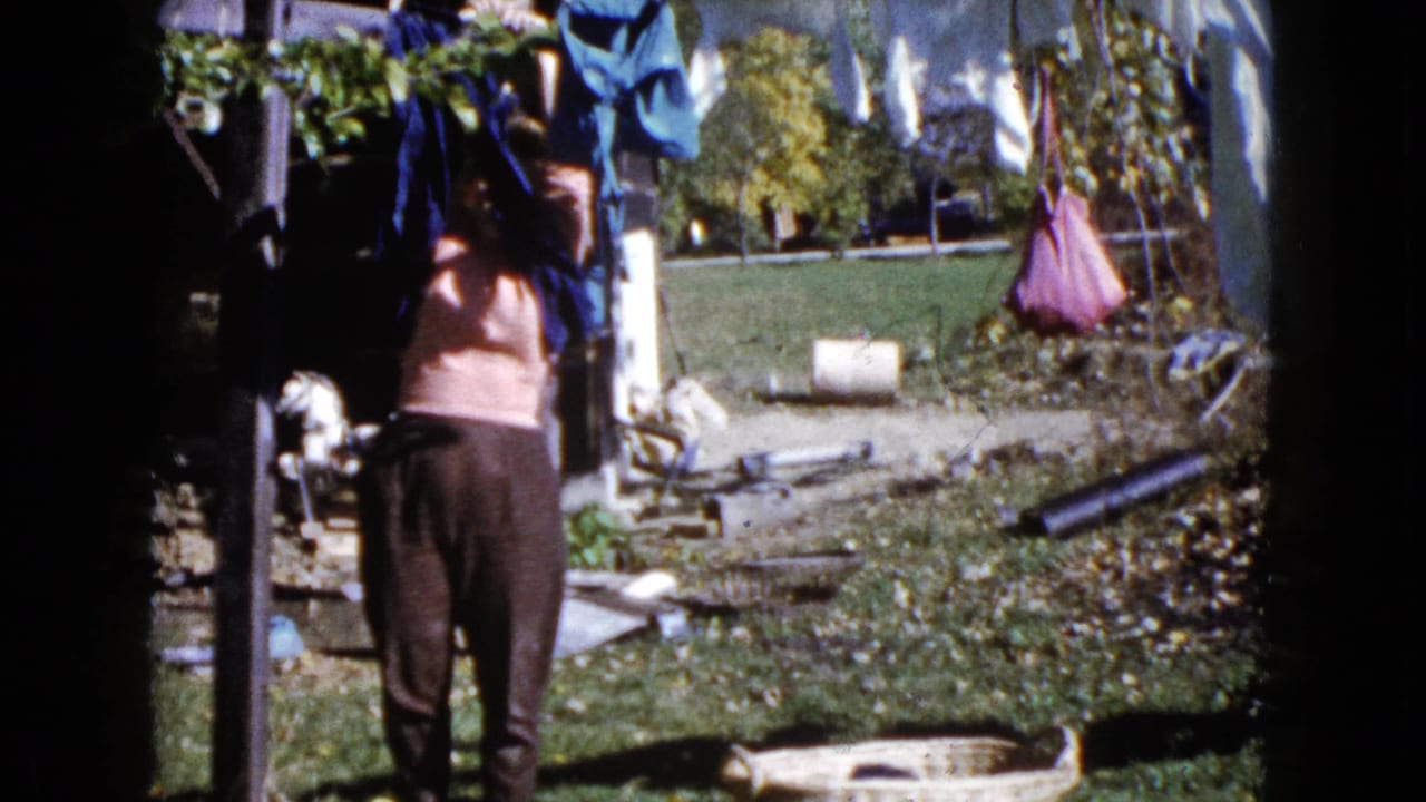 Woman reaches toward laundry hanging from a backyard clothesline.