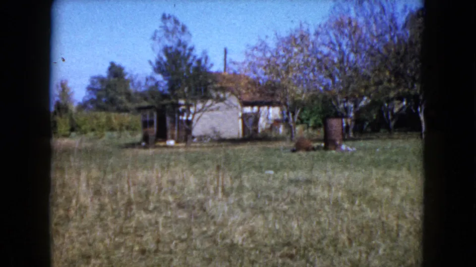 Rural 1960 Wauconda frame showing a modest farmhouse, trees, open grass, and a barrel-like yard object.