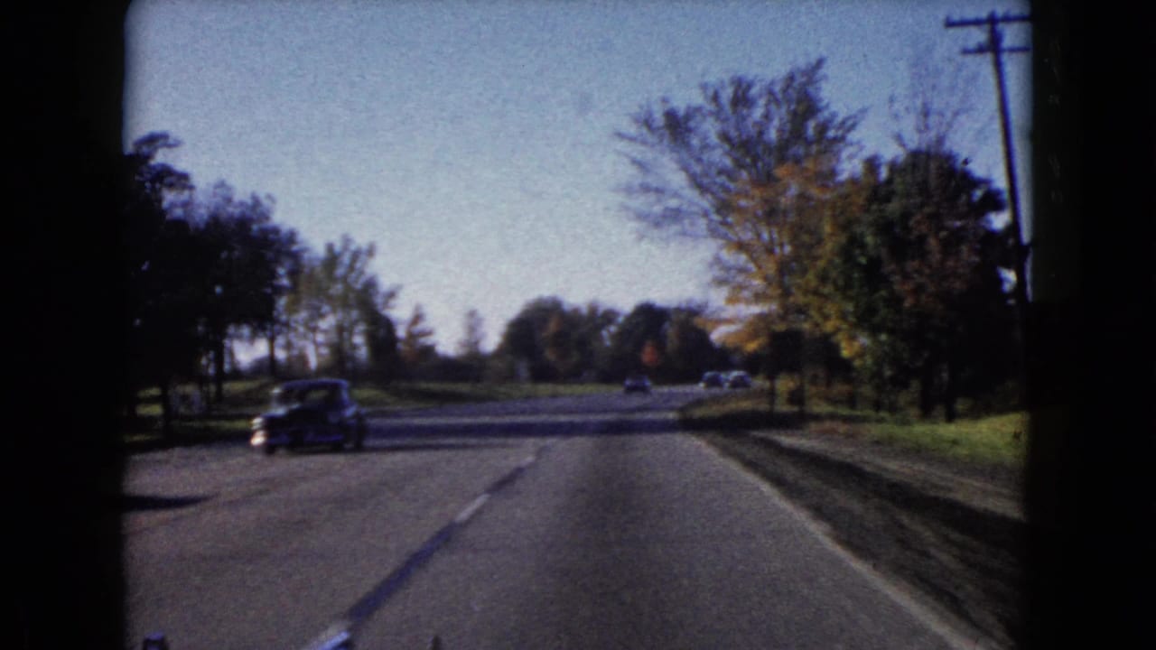 Forward-facing 8mm road scene in Wauconda, Illinois, showing a paved lane, roadside trees, utility poles, and passing cars.