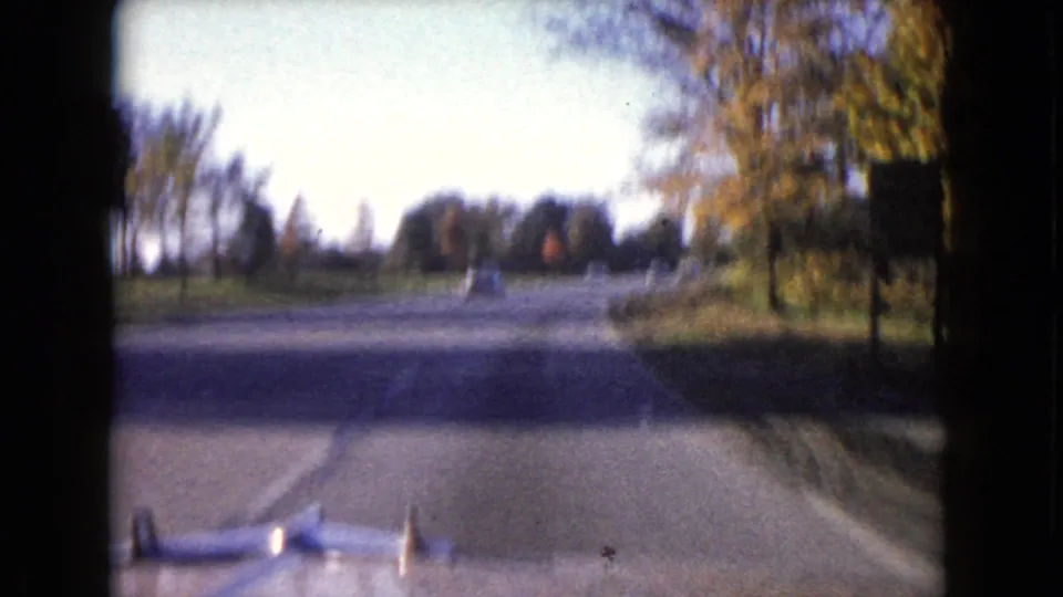 Soft, motion-blurred 8mm driving view on a Wauconda road, with autumn trees, a roadside sign, and the vehicle hood at the bottom edge.