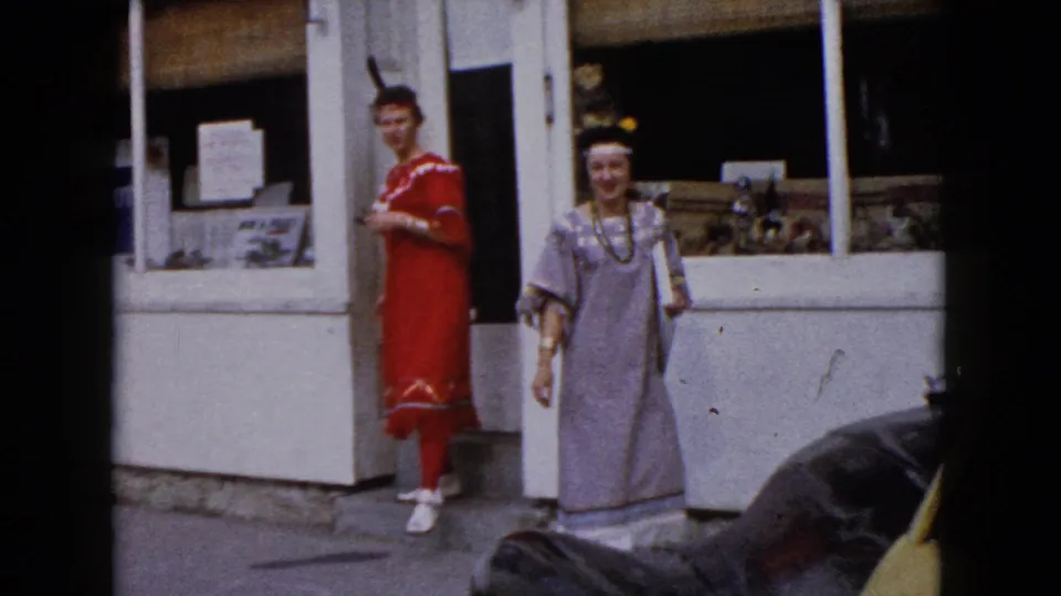 In Wauconda, Illinois, two women in Native American-inspired costumes stand outside a white storefront in 1960 home-movie footage.