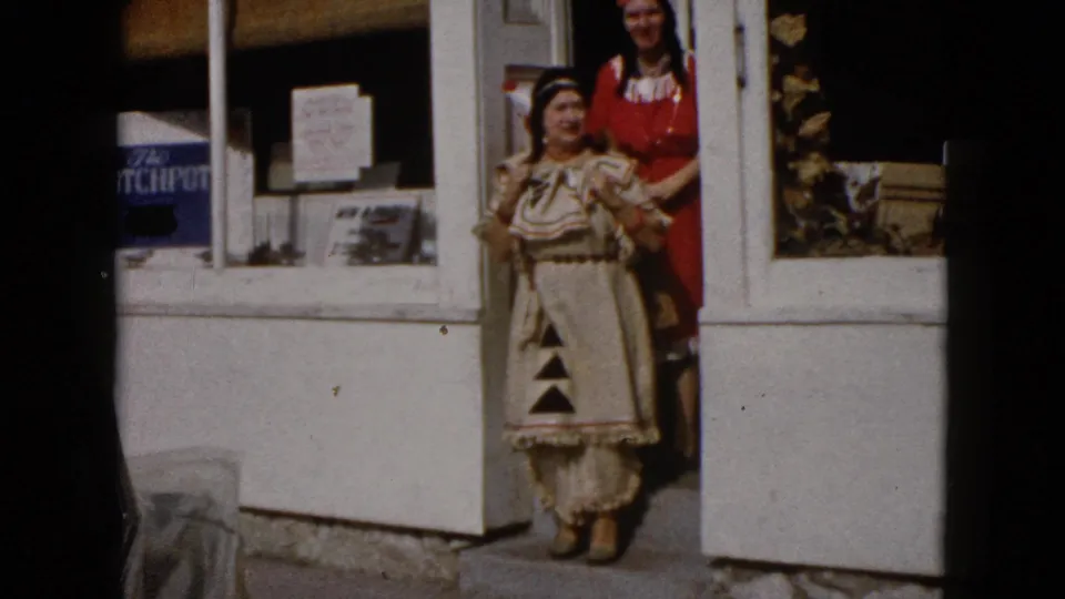 Two costumed women stand at the Wauconda storefront doorway, one in a patterned dress and another in red behind her.