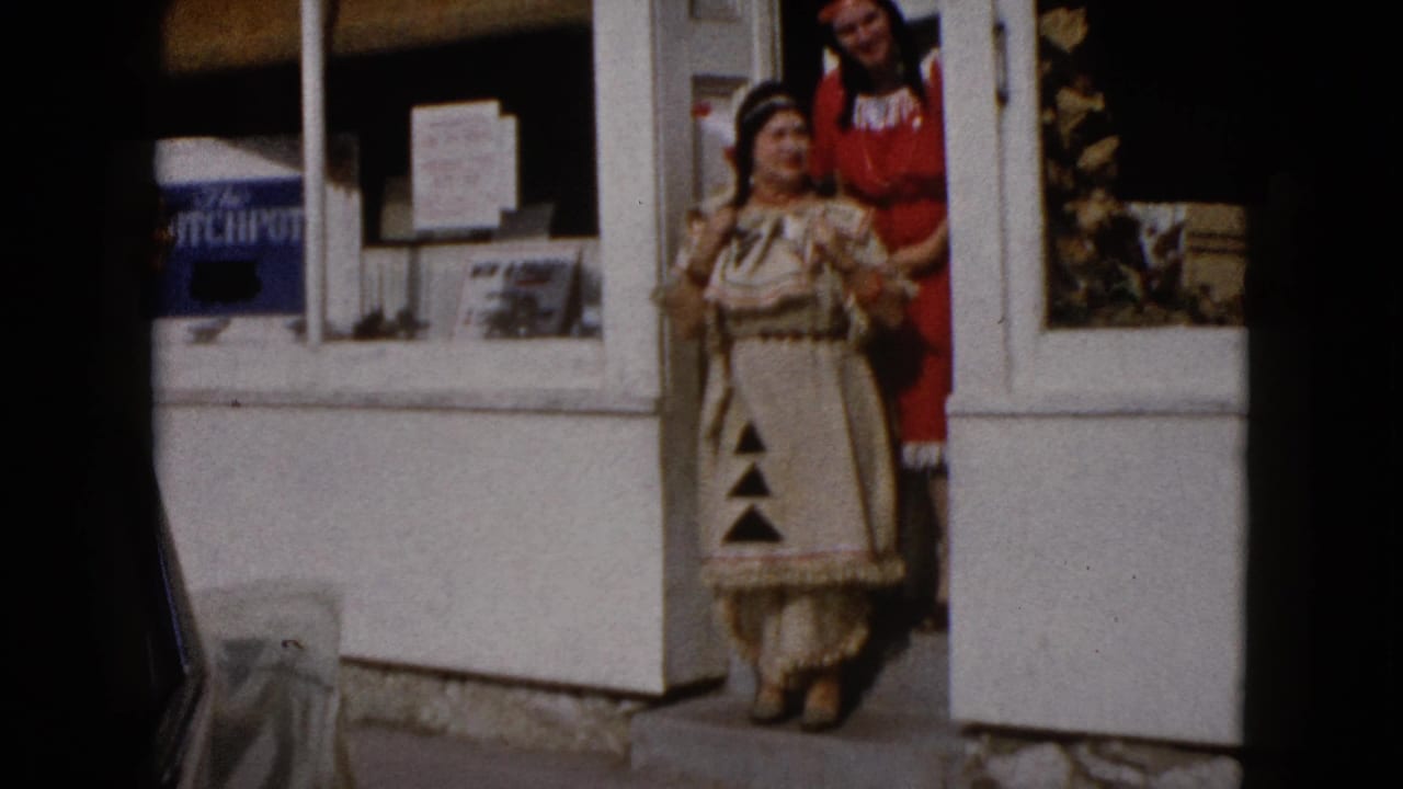 Two costumed women stand outside a white storefront doorway.