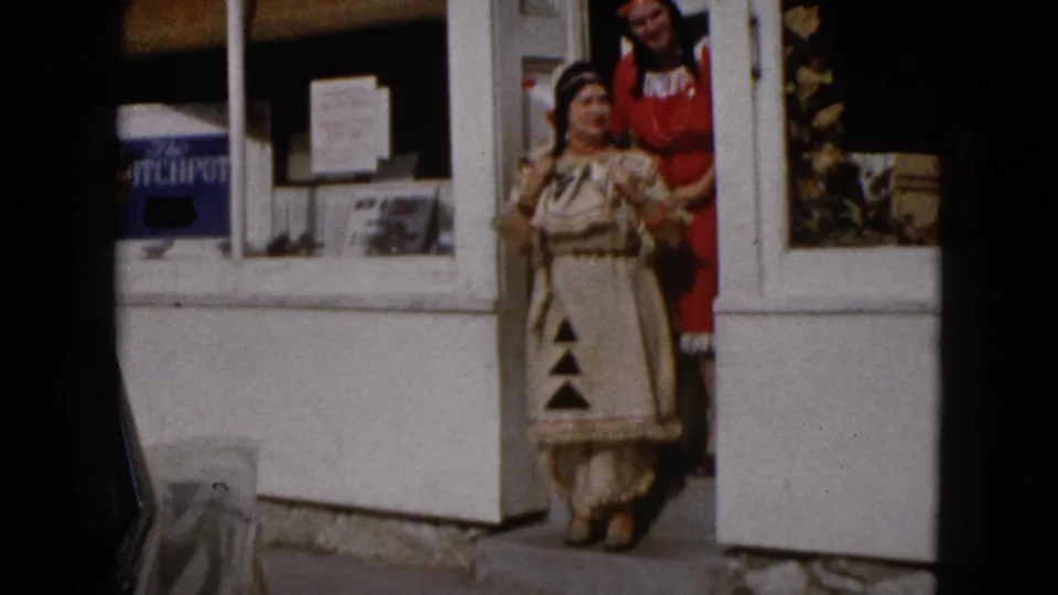 In 1960 Wauconda, Illinois footage, two women in Native American-inspired attire pose outside a white storefront.
