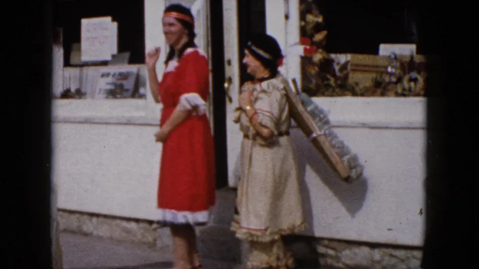 At the end of the Wauconda clip, the women in red and beige costumes stand side by side near the storefront and gesture toward the camera.