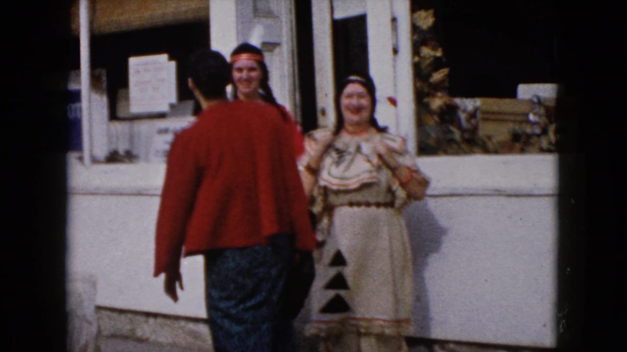 A woman in a red sweater faces two costumed women beside a storefront window.