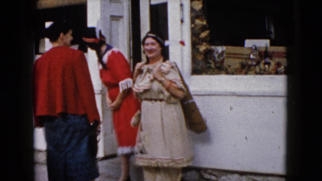 1960 Wauconda home-movie frame with three adult women near a storefront, including two in Native American-inspired outfits.