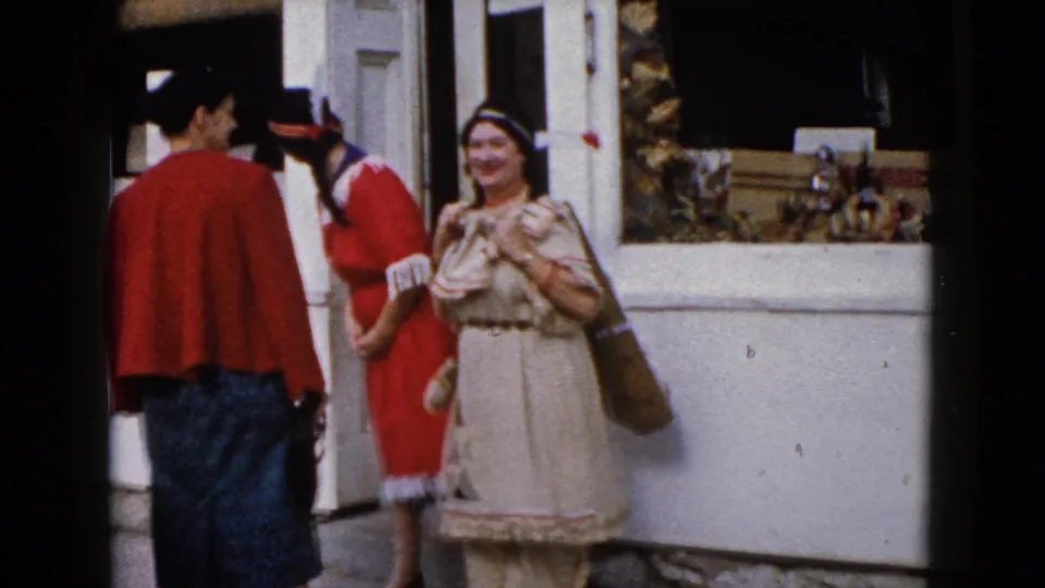 1960 Wauconda home-movie frame with three adult women near a storefront, including two in Native American-inspired outfits.